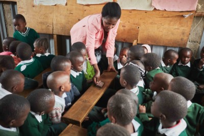 A teacher in Kenya wearing a pink blouse interacts with her students while using the EIDU app in the classroom.