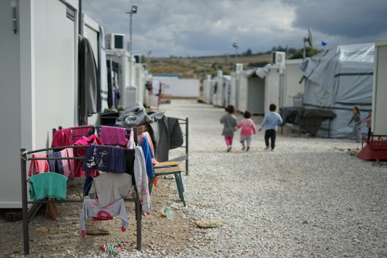 Three children walk away from the camera at a refugee camp
